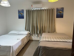 Ett rum med två sängar, en gardin, en luftkonditioneringsanläggning och två tavlor med havssköldpaddor som hänger på väggen.