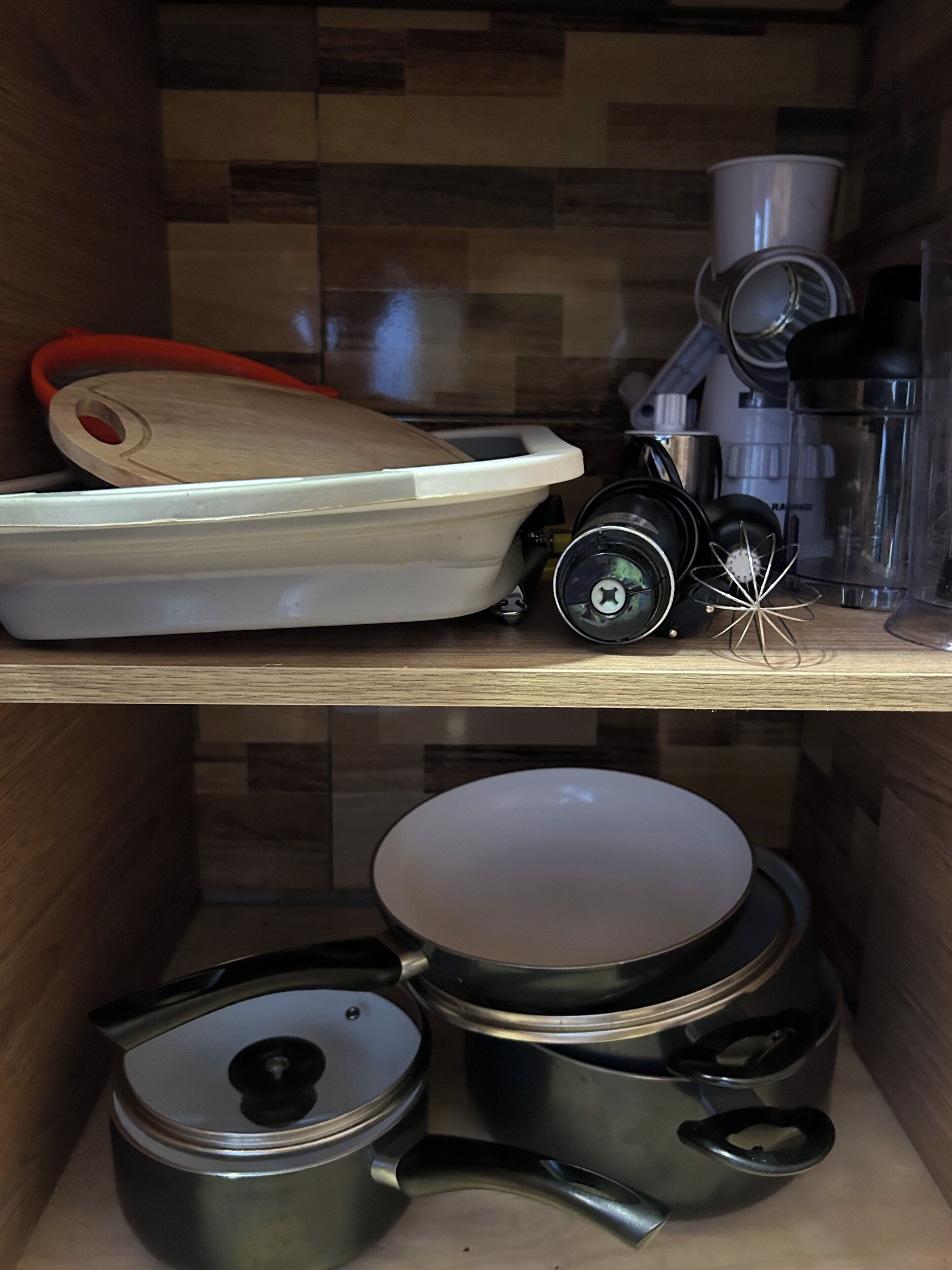 Een keuken met een houten plank waarop een waterkoker, een koffiezetapparaat en een waterkoker staan. Daaronder bevinden zich pannen en braadpannen op een lager gelegen plank.