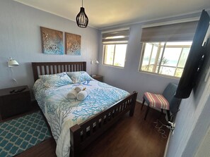 Een slaapkamer met een bed, nachtkastjes, een televisie, kunstwerken en een raam.