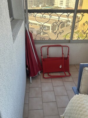 A balcony with a red chair, a red umbrella, and a view of a cityscape. - Breathtaking Views on Avenida del Mar (La Serena)