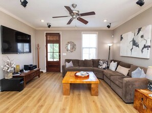 A living room with a ceiling fan, a flat-screen TV, a wooden coffee table, a brown sofa, and a large abstract painting. - The Trophy Room at Tanglewood | Walk to Square (Oxford)