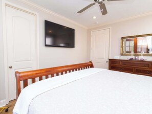 Een slaapkamer met een bed, een dressoir, een televisie en een plafondventilator.