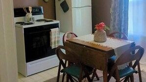 Cocina compacta con estufa, horno, microondas y refrigerador. Hay una mesa de comedor con sillas y un florero con flores.