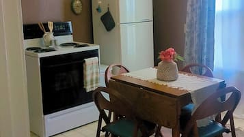 Et kompakt køkken med komfur, ovn, mikroovn og køleskab. Der er et spisebord med stole og en vase med blomster.