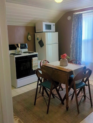 A compact kitchen with a stove, oven, microwave, and refrigerator. There is a dining table with chairs and a vase with flowers. - Welcome to The Cozy Upstairs Retreat—a peaceful, centrally located getaway (Rapid City)