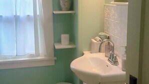 Un baño con un lavamanos blanco, un espejo, una cesta y una ventana con cortina.