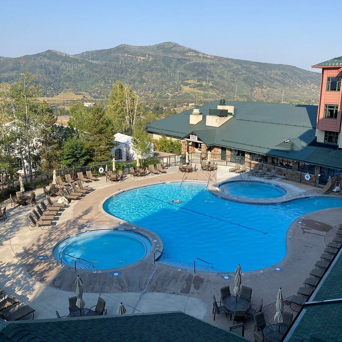 A resort with a large pool area, lounge chairs, and a view of mountains.