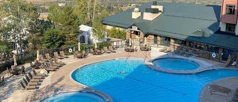 A resort with a large pool area, lounge chairs, and a view of mountains.