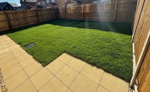 A backyard with a wooden fence, a paved patio, and a well-maintained lawn. - Stylish modern double room with private bathroom (Peterborough)