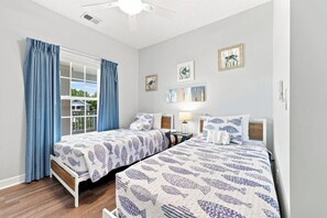 Une chambre avec deux lits, une fenêtre avec des rideaux et des œuvres d’art mural.