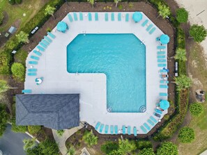 Vue aérienne d’une piscine dotée de plusieurs espaces de détente et entourée de verdure.