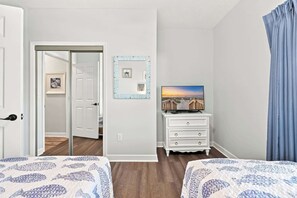 Ein Hotelzimmer mit zwei Betten, einem Fernseher auf einer Kommode und einer Tür zu einem weiteren Raum.