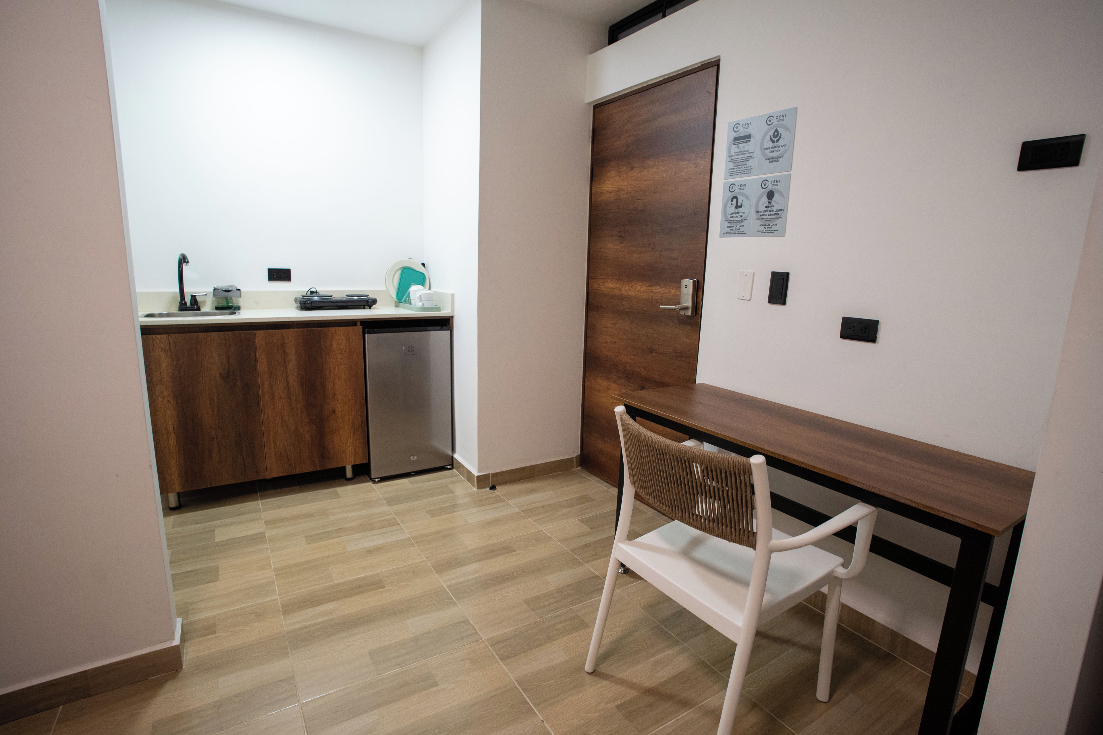 A modern kitchen with a wooden cabinet, a sink, and a countertop. There is a white chair and a wooden table in the foreground.