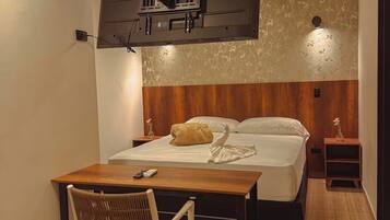 Una habitación de hotel con una cama, mesita de noche, una silla y un televisor montado en la pared.