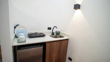 Cozinha compacta com máquina de lavar louça embutida, pia e bancada com chaleira e pequeno eletrodoméstico.