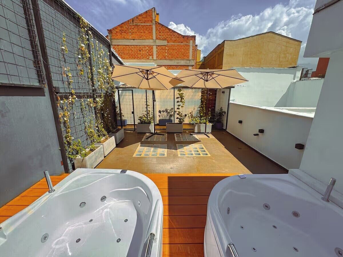 Un patio en la azotea con dos jacuzzis, mobiliario exterior y vistas de la ciudad.