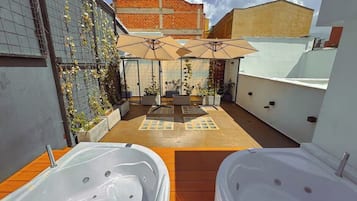 Un patio en la azotea con dos jacuzzis, mobiliario exterior y vistas de la ciudad.