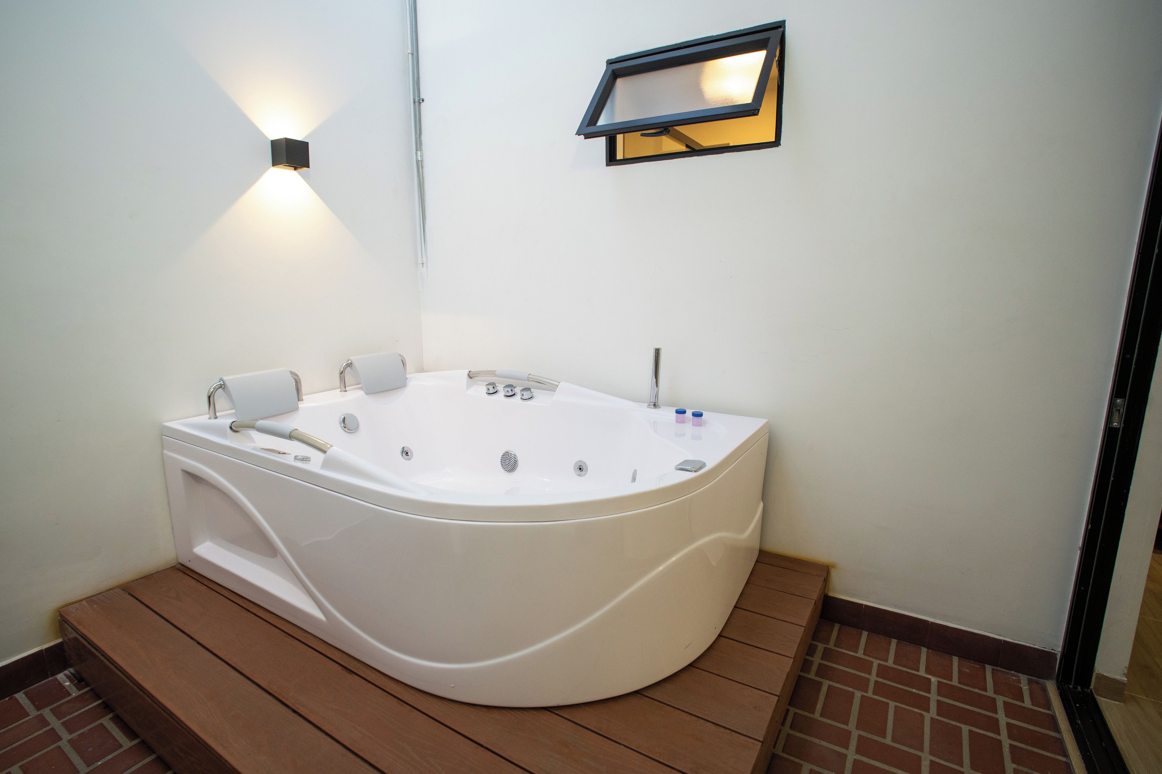 A modern bathroom with a freestanding bathtub, a wall-mounted light fixture, and a small shelf.