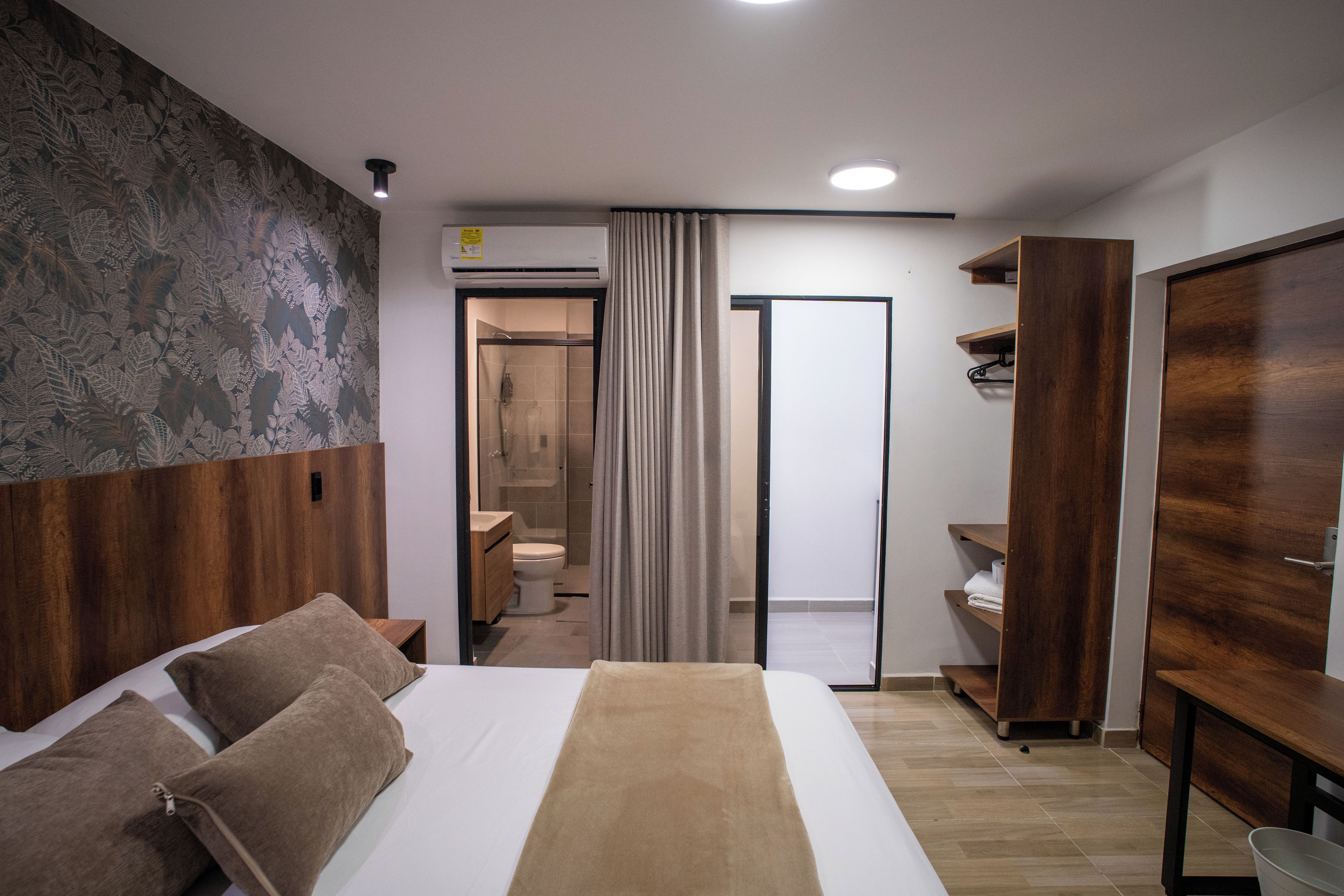 A modern hotel room with a large bed, a wooden wardrobe, a bathroom with a shower, and a curtain.
