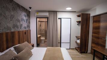 A modern hotel room with a large bed, a wooden wardrobe, a bathroom with a shower, and a curtain.