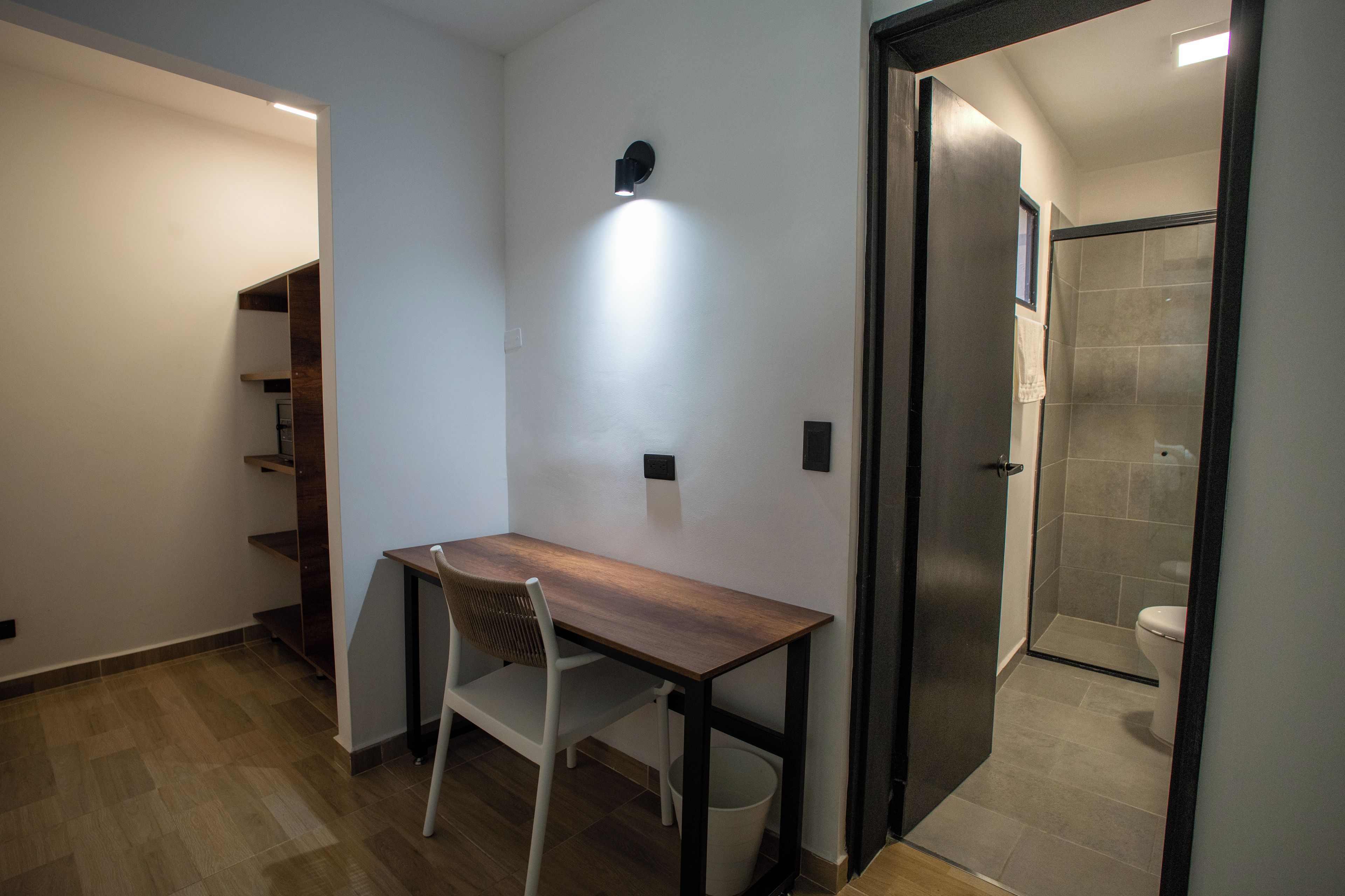 A small, modern bathroom with a shower, toilet, and a wooden desk with a chair.