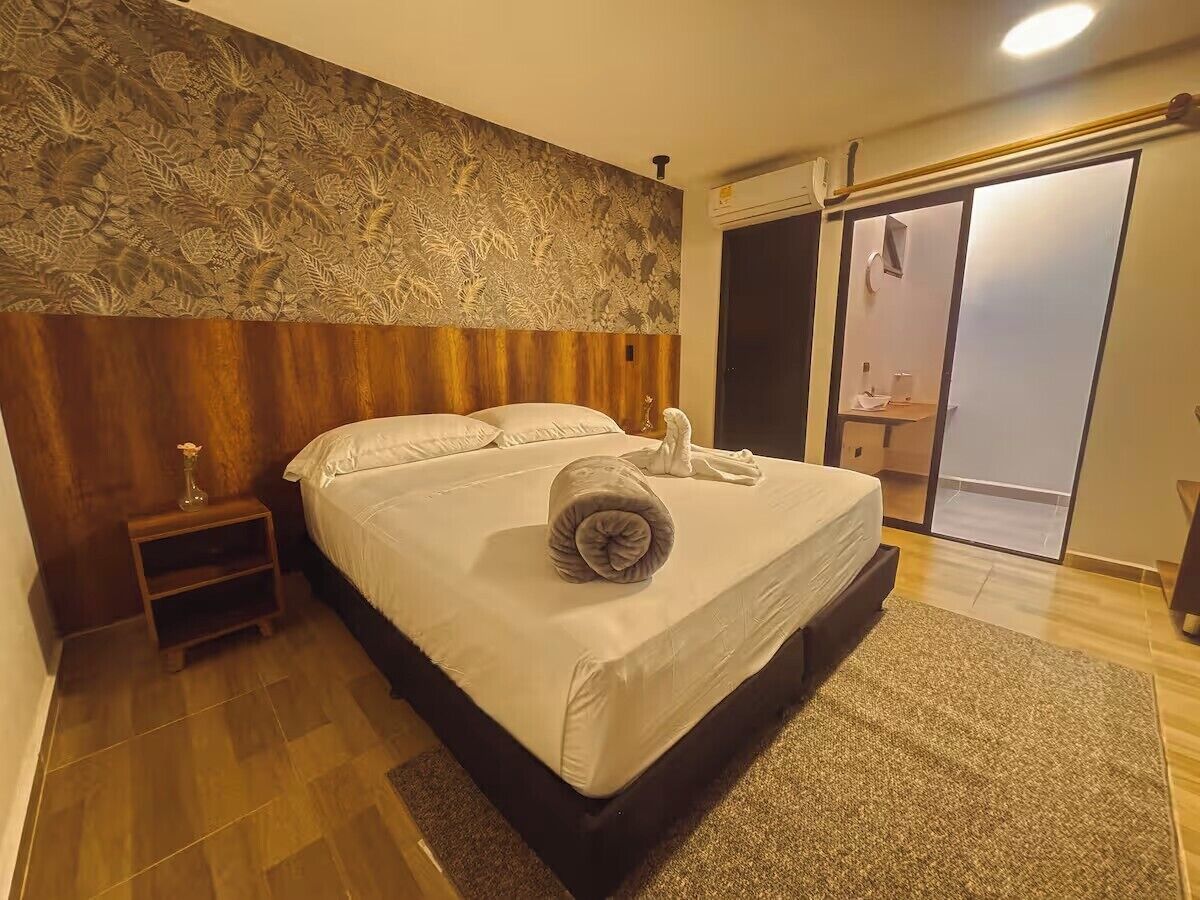 Habitación de hotel con una cama grande, una mesita de noche, un adorno en la pared y una puerta corrediza a un balcón.