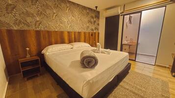 Habitación de hotel con una cama grande, una mesita de noche, un adorno en la pared y una puerta corrediza a un balcón.