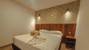 Habitació d'hotel amb un llit gran, un panell de fusta al capçal, una tauleta de nit i un ram de flors.