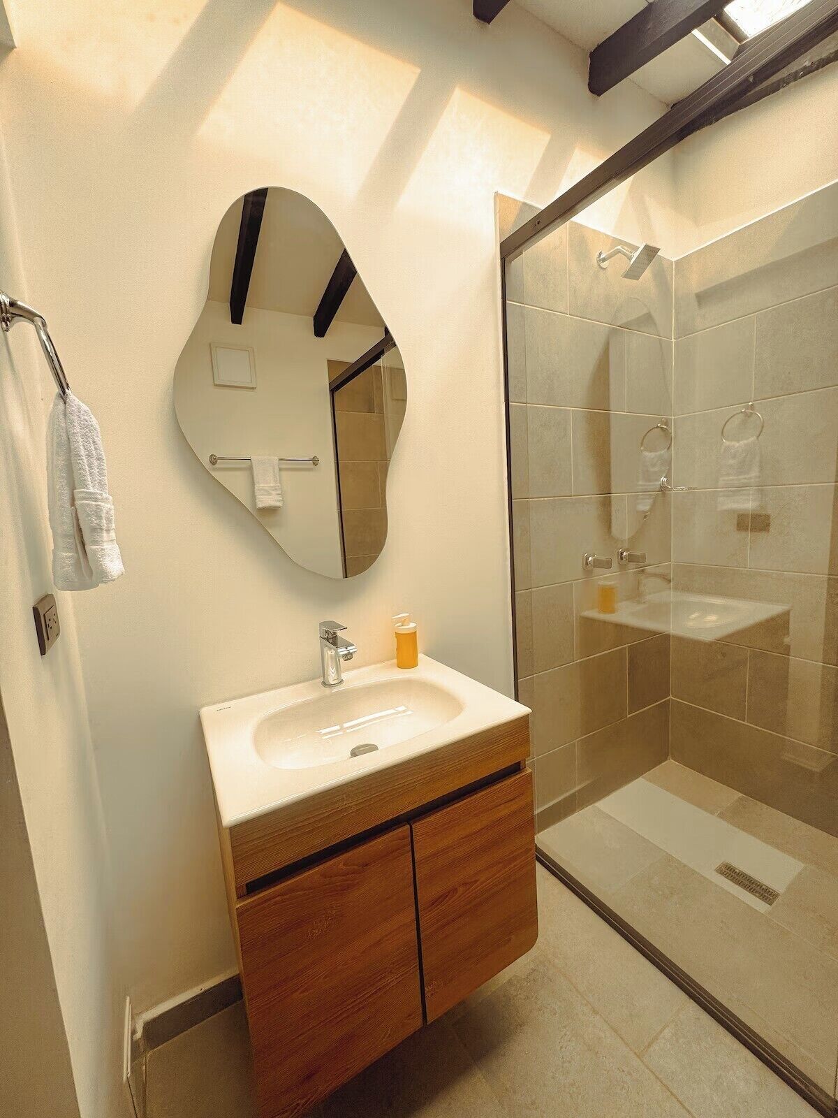 Un baño con tocador de madera, espejo redondo, cabina de ducha de vidrio y toallero.