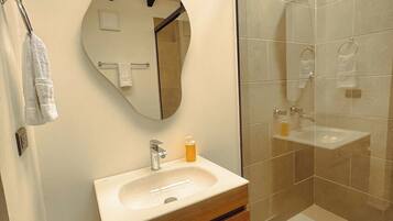 Un baño con tocador de madera, espejo redondo, cabina de ducha de vidrio y toallero.