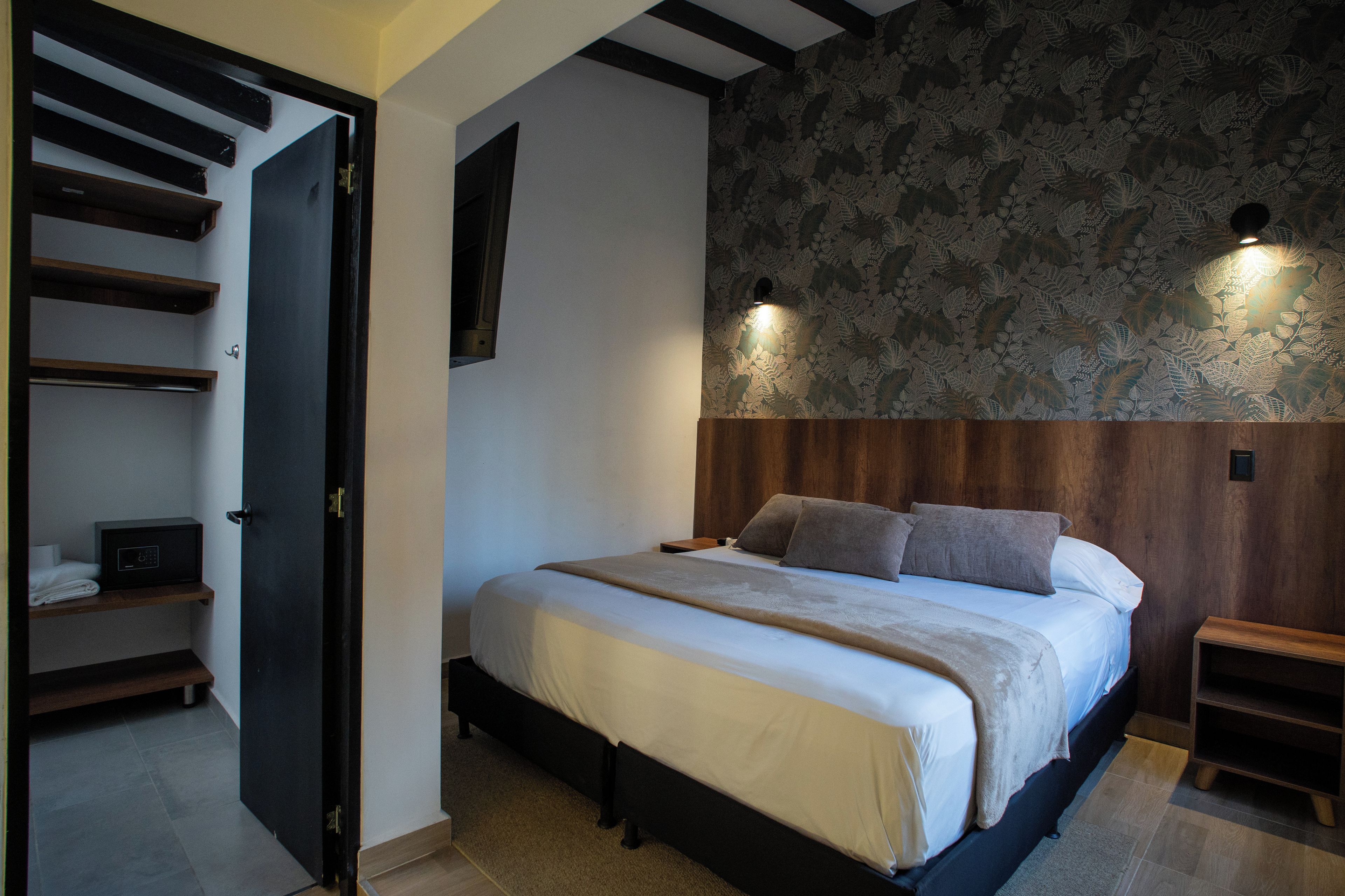 A bedroom with a bed, a nightstand, a wall-mounted light, and a door leading to a staircase.