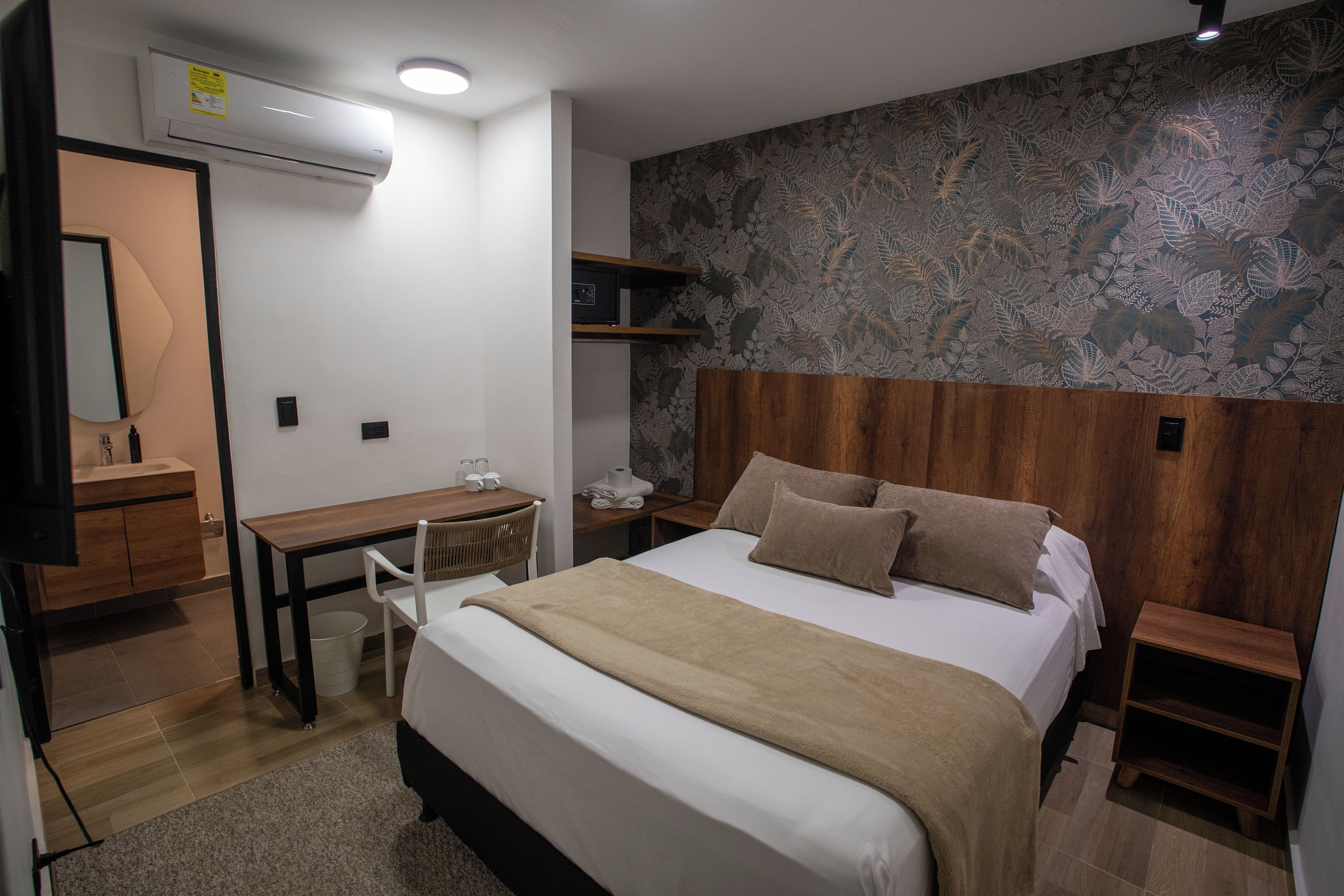 A hotel room with a bed, bedside tables, a desk, a chair, a wardrobe, and a mirror.