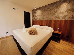 Habitación de hotel con una cama, una mesita de noche, una pared con diseño de hojas y una puerta.