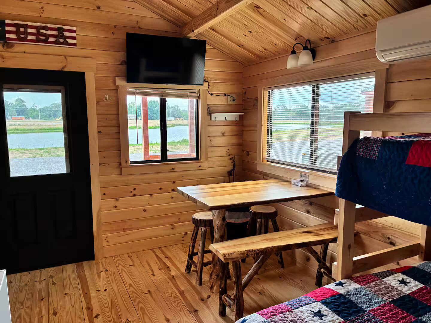 A cabin interior with a wooden interior, a table, stools, a bunk bed, and a TV mounted on the wall.
