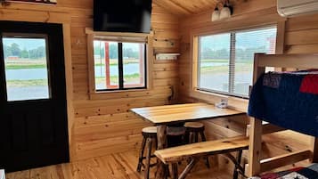A cabin interior with a wooden interior, a table, stools, a bunk bed, and a TV mounted on the wall.