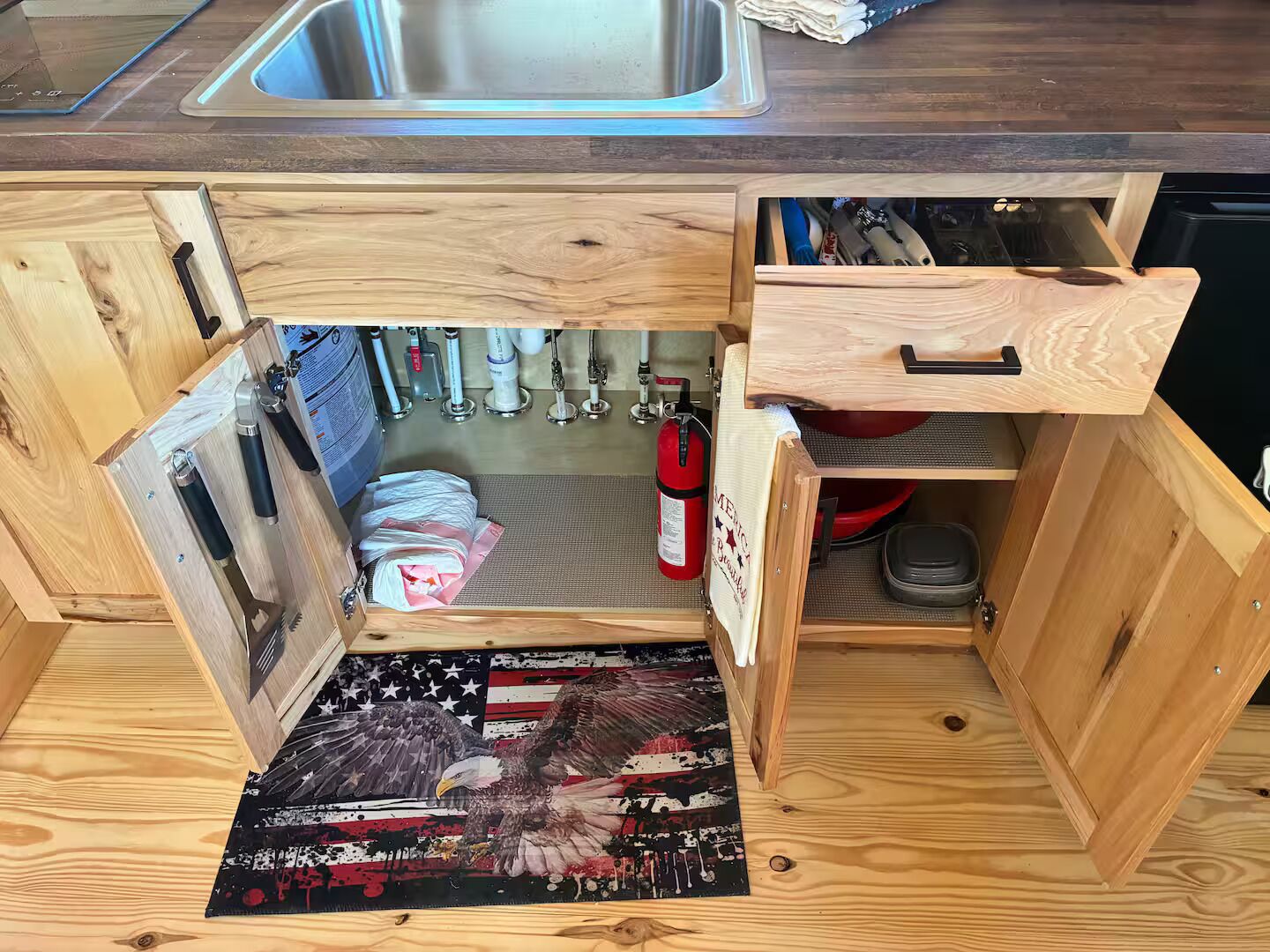 A kitchen with wooden cabinetry, a stainless steel sink, and various kitchen utensils.