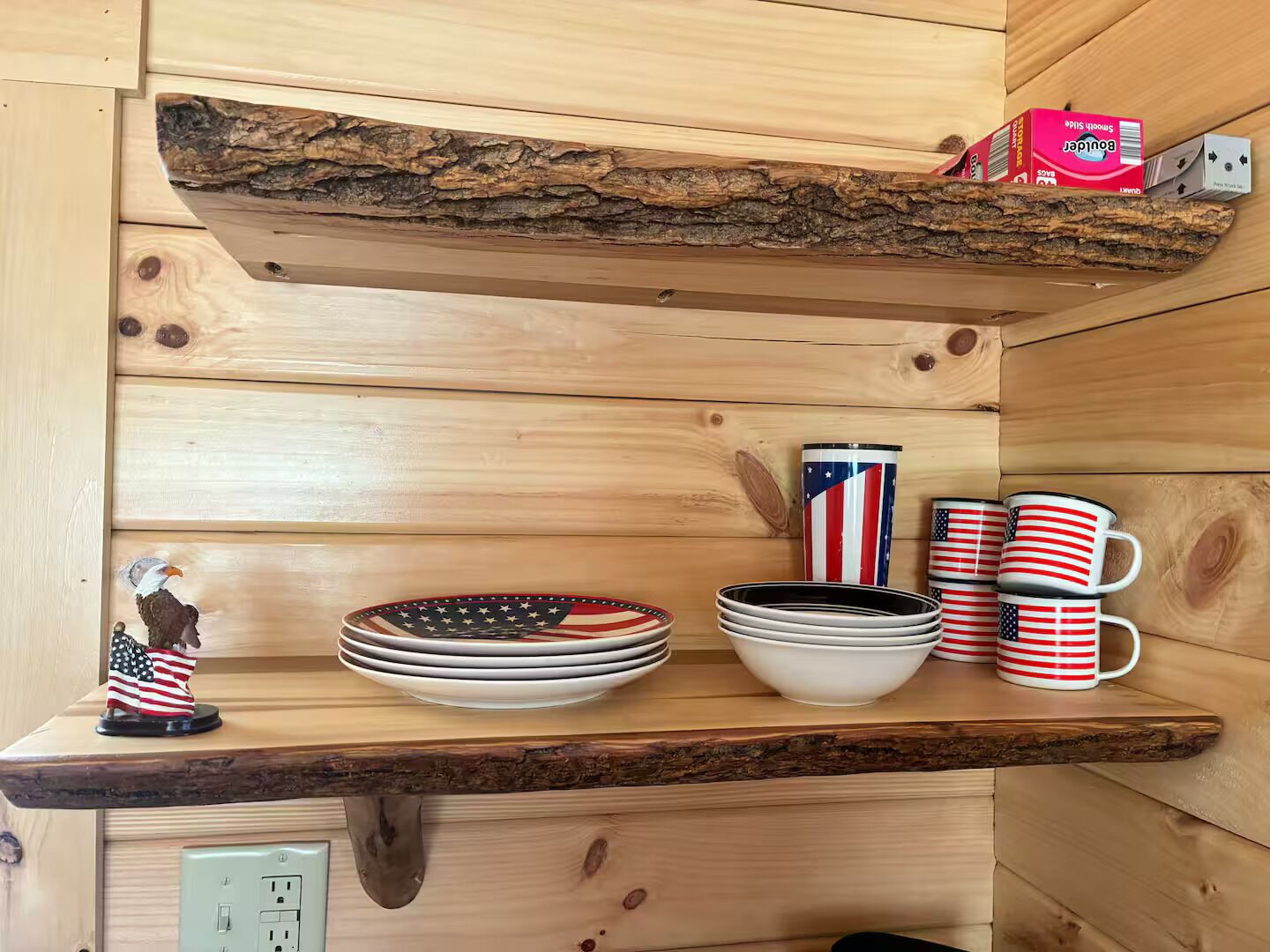 Un estante de madera con diseño rústico que sostiene platos, tazones y tazas con diseños de la bandera estadounidense.