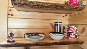 A wooden shelf with a rustic design, holding plates, bowls, and mugs with American flag patterns.