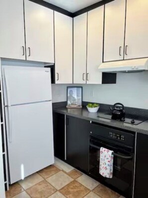 A compact kitchen with white cabinets, a black countertop, a white refrigerator, a dishwasher, and a kettle. - Location, location location! (Seattle)