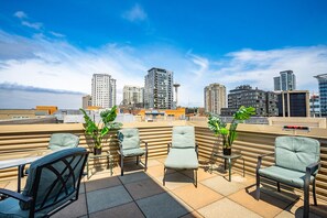 A rooftop terrace with multiple seating areas, potted plants, and a city skyline in the background. - Location, location location! (Seattle)