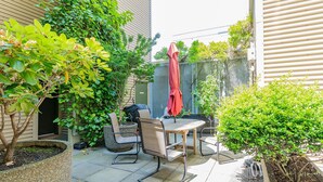 A patio with a table and chairs, surrounded by greenery and a red umbrella. - Location, location location! (Seattle)