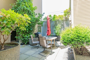 A patio with a table and chairs, surrounded by greenery and a red umbrella. - Location, location location! (Seattle)