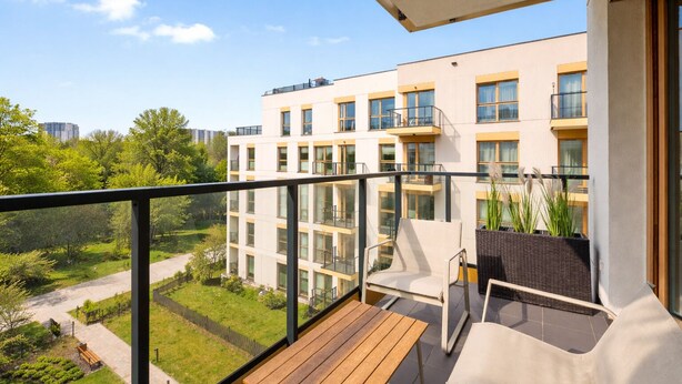 Un balcon avec une table et des chaises en bois, donnant sur un jardin et un immeuble doté de nombreuses fenêtres.