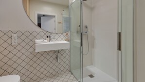 Une salle de bain moderne avec une douche à parois de verre, un lavabo blanc et un mur recouvert de carreaux à motifs.