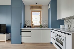 Cozinha compacta com armários brancos, forno Bosch, cafeteira e janela com vista para edifícios.