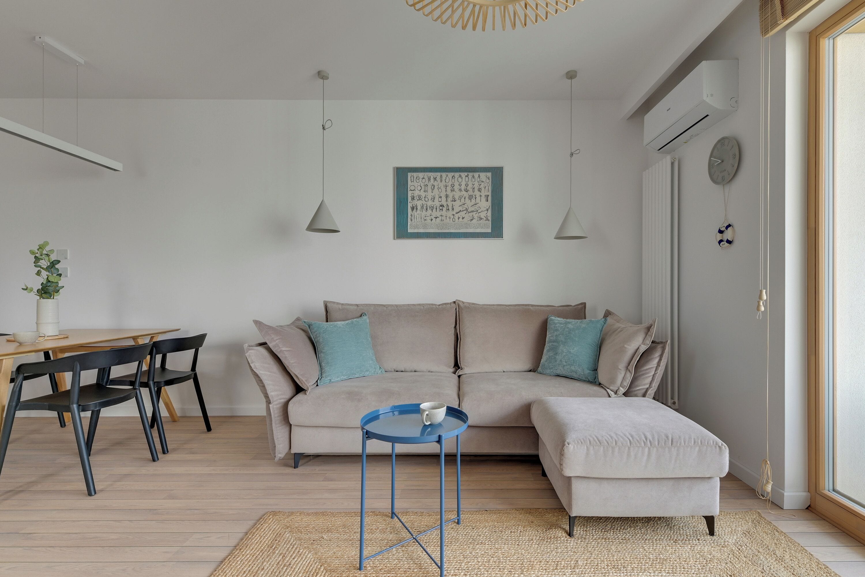 A modern living room with a sofa, a small table, and a dining area with chairs.