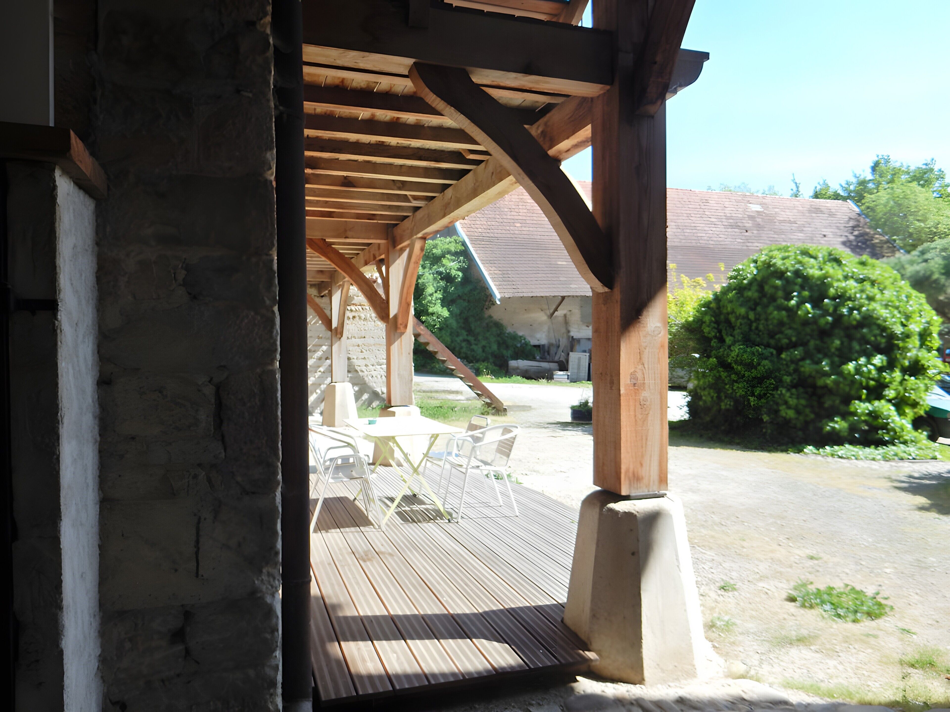 A wooden deck with outdoor furniture, a stone wall, and a covered area with a view of a house and greenery.