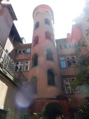 A multi-story building with a central tower, balconies, and windows. - “Le Chapuis - Gîtes Notre Dame De Confort” Apartment with Balcony and Shared Garden (Jons)