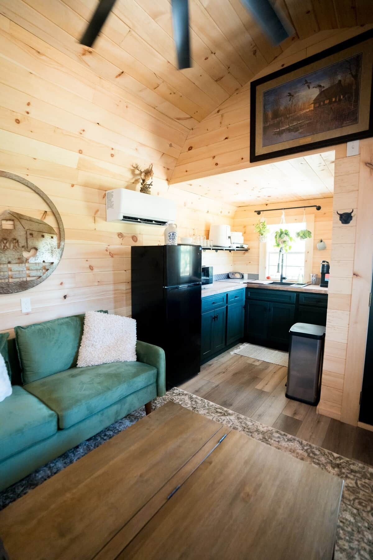 Un interior de cabaña acogedor con kitchenette, un sofá verde y piso de madera.