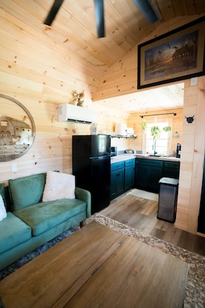 A cozy cabin interior with a kitchenette, a green sofa, and a wooden floor.